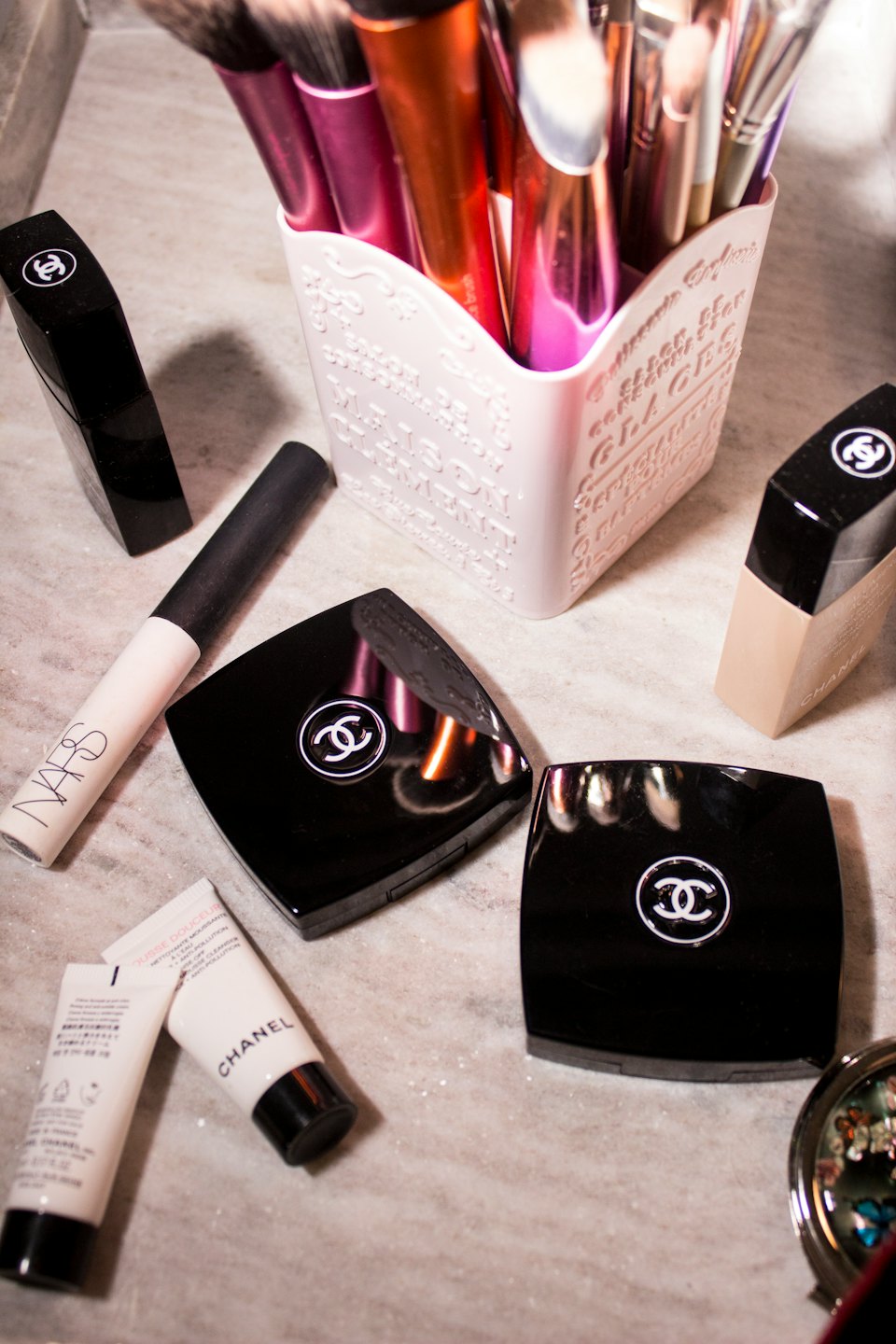 Luxury makeup products and brushes on a marble countertop.