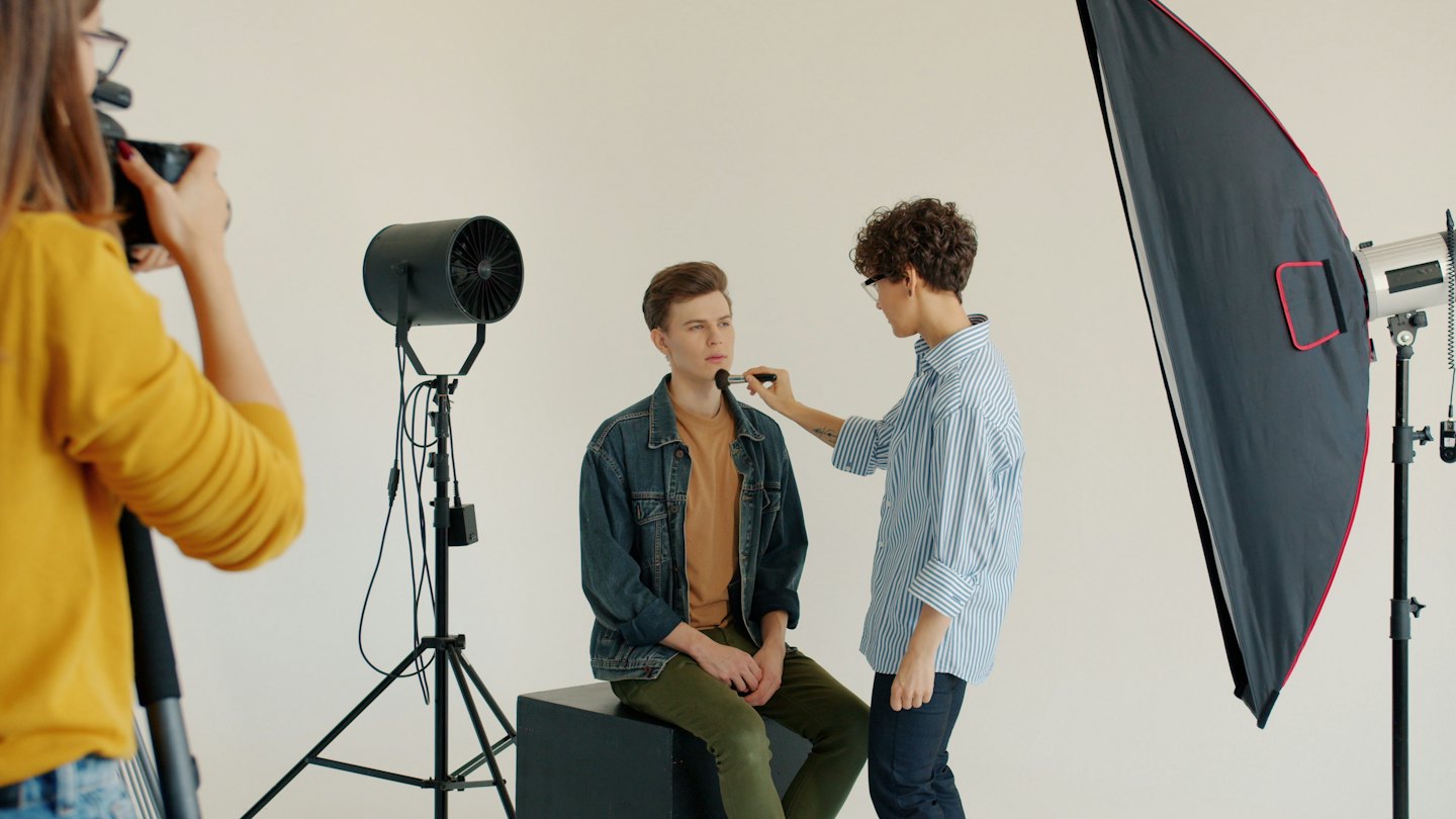 Makeup artist applies foundation to model's chin during photoshoot.